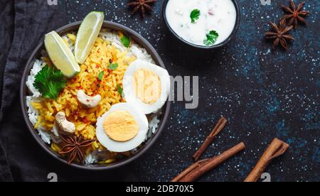 Indian Egg Biryani o da una vista dall'alto su sfondo scuro. Biryani all'uovo - riso Basmati cotto con uova arrosto e spezie masala, servito con yogurt Foto Stock