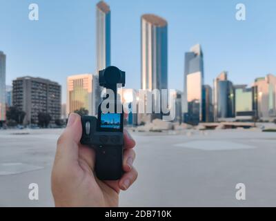 Un uomo che tiene la tasca DJI Osmo, una piccola macchina fotografica d'azione con un gimbal - vlog di ripresa in città | Abu Dhabi skyline e punti di riferimento Foto Stock