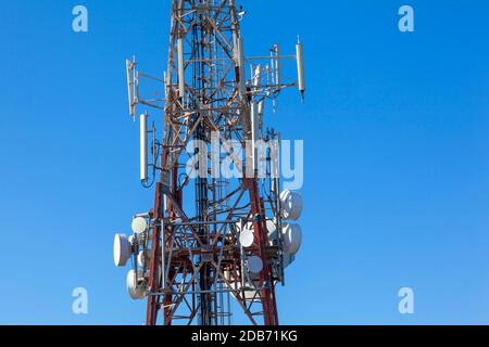 primo piano dell'albero delle telecomunicazioni che mostra varie antenne e piatti contro il cielo blu chiaro Foto Stock