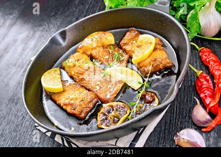 Salmone rosa con salsa di miele, succo di limone, aglio, pepe caldo e salsa di soia, fette di limone e un rametto di timo in una padella su asciugamano, prezzemolo Foto Stock