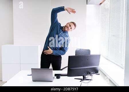 Giovane Imprenditore facendo esercizio di stretching in ufficio Foto Stock
