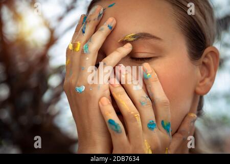 Closeup foto di una ragazza sognante con occhi chiusi e mani colorate in vernice, artista moderno, foto concettuale di una generazione con nuove idee Foto Stock