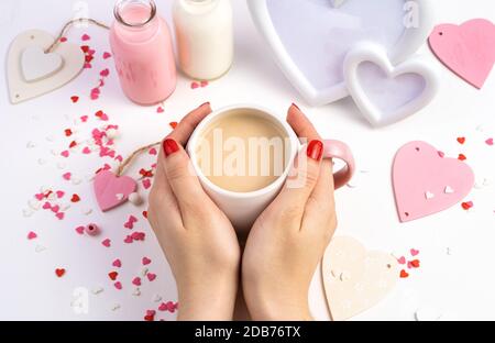 Una tazza di caffè con latte nelle mani di una donna su uno sfondo di cuori su uno sfondo bianco. Foto Stock