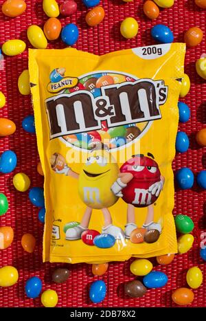 M&MS Retail Packaging con caramelle colorate sfuse in un appartamento posare la vita morta su uno sfondo tessile rosso Foto Stock