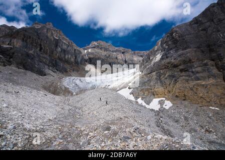 Due scalatori sull'avvicinamento al crinale NE del Monte Assiniboine cammina su per una gmorraine prima di attraversare un ghiacciaio nel soleggiato giorno d'estate. Foto Stock