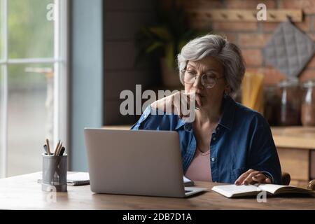 Donna matura seria che indossa gli occhiali che lavorano sul laptop online Foto Stock