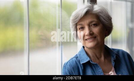 Ritratto della testa sorridente donna matura in piedi vicino alla finestra Foto Stock