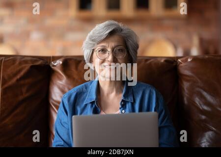 Ritratto della testa sorridente donna matura indossando occhiali che tengono un computer portatile Foto Stock
