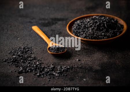 Una ciotola di legno e un cucchiaio riempito con cristalli di sale nero Himalayan Foto Stock