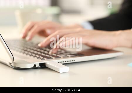 Primo piano delle mani di una donna executive utilizzando un computer portatile con un pendrive collegato seduto su una scrivania in ufficio Foto Stock