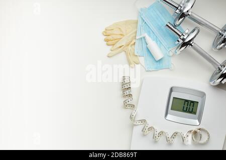 Attrezzature sportive, bilance, maschere mediche e igienizzatore su sfondo bianco. Vista dall'alto, spazio di copia. Fitness. Periodo di isolamento. Peso e controllo della salute Foto Stock