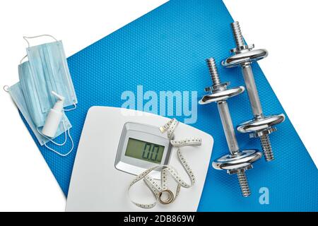 Attrezzature sportive, bilance, maschere mediche e igienizzatore su sfondo bianco. Vista dall'alto, spazio di copia. Fitness. Periodo di isolamento. Peso e controllo della salute Foto Stock