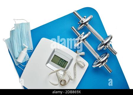 Attrezzature sportive, bilance, maschere mediche e igienizzatore su sfondo bianco. Vista dall'alto, spazio di copia. Fitness. Periodo di isolamento. Peso e controllo della salute Foto Stock