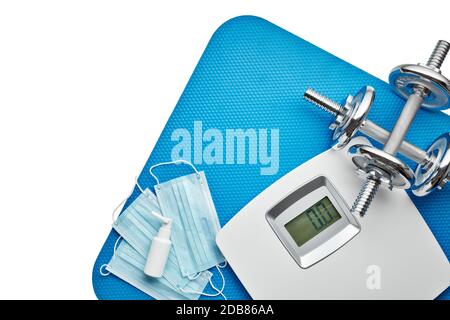 Attrezzature sportive, bilance, maschere mediche e igienizzatore su sfondo bianco. Vista dall'alto, spazio di copia. Fitness. Periodo di isolamento. Peso e controllo della salute Foto Stock