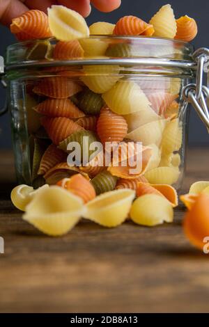 Pasta di Conchiglie colorata in vaso di vetro su sfondo di legno. Vista frontale, primo piano. Foto Stock