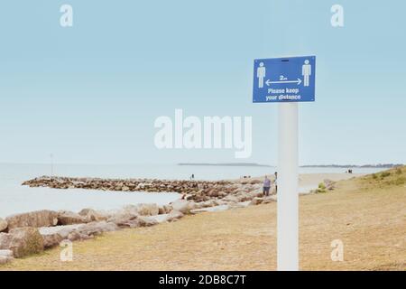 Messaggio con si prega di mantenere la distanza sul cartello in piedi sulla spiaggia. Nuove normali misure di distanziamento sociale nei luoghi pubblici durante un Covid-19 Foto Stock