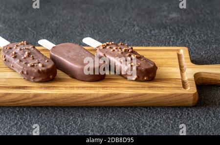 Gelaterie alla vaniglia ricoperte di cioccolato sulla tavola di legno Foto Stock