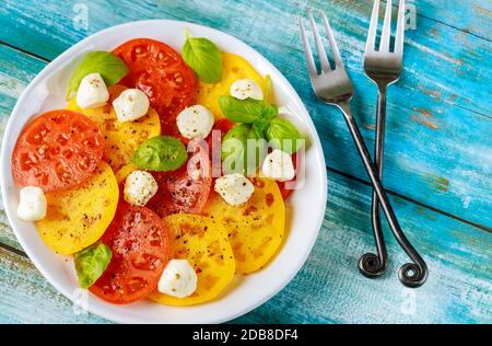 Condire il pomodoro a fette con mozzarella, basilico su piatto con forchetta. Vista dall'alto. Foto Stock