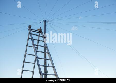 Cablaggio elettrico sul tetto di un alto edificio, una doppia scala contro il cielo blu. Spazio di copia Foto Stock