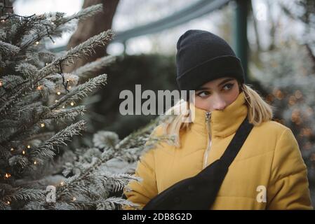 Ritratto di una giovane donna in una giacca di puffer in piedi presso un albero di Natale, Francia Foto Stock