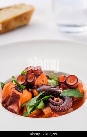 Stufato di calamari di polpo con salsa di tomatoe in un piatto con pane e bicchiere d'acqua Foto Stock