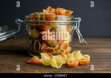 Pasta di Conchiglie colorata in vaso di vetro su sfondo di legno. Vista frontale, primo piano. Foto Stock