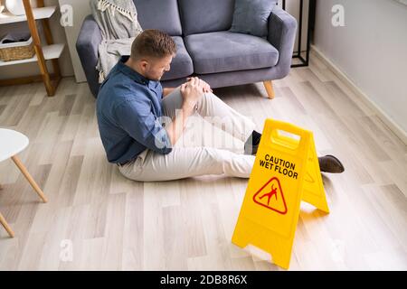 Uomo che cade sul pavimento bagnato di fronte al cartello di attenzione a casa Foto Stock