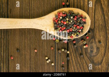 Pepe multicolore su un cucchiaio di legno e cosparso fianco a fianco su un tavolo di legno. Viste dall'alto con spazio libero. Foto Stock