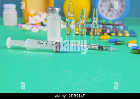 Siringa con fiale di vetro e farmaci pillole farmaco. Sullo sfondo c'è una scatola di legno e una mela gialla. Vista frontale. Foto Stock