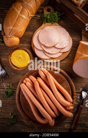 Vista dall'alto delle fette di carne deli e delle salsicce Frankfurter servite con senape su sfondo di legno d'epoca Foto Stock