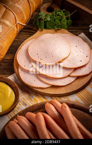 Prodotti a base di carne fredda e salsicce di cane caldo su tagliere di legno Foto Stock