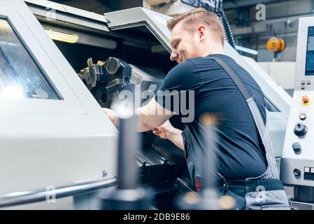 Operatore esperto che cambia la configurazione dell'utensile del tornio sul pavimento della fabbrica Foto Stock