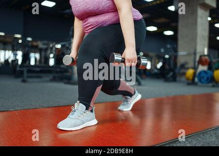 Donna in sovrappeso che fa esercizio con manubri in palestra, allenamento attivo. La persona femminile obesa lotta con il peso in eccesso, allenamento aerobico contro le obe Foto Stock