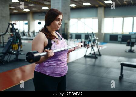 Donna sovrappeso posa con manubri su brench in palestra, allenamento attivo. La persona femminile obesa lotta con il peso in eccesso, allenamento aerobico contro obe Foto Stock