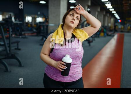 Donna in sovrappeso drink dieta cocktail in palestra, allenamento attivo. La persona femminile obesa lotta con il peso in eccesso, allenamento aerobico contro l'obesità, la spor Foto Stock