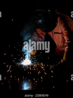 Gli operai dell'industria del metallo stanno saldando le lamiere di acciaio per i progetti immobiliari ricevuti. Sparkler su sfondo nero, primo piano. Lavori pesanti in fabbrica. Foto Stock