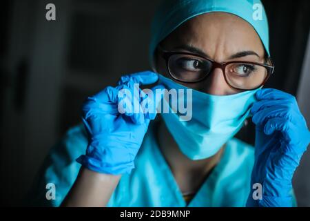 Primo piano di una donna medico che regola la sua maschera chirurgica e occhiali, in luce naturale. Foto Stock