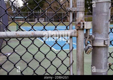 Il cancello di un campo da tennis è chiuso con una rete da tennis in background. Foto Stock