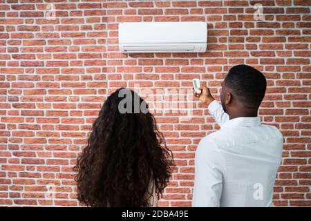 Felice Coppia giovane la regolazione della temperatura del condizionatore aria da remoto Foto Stock
