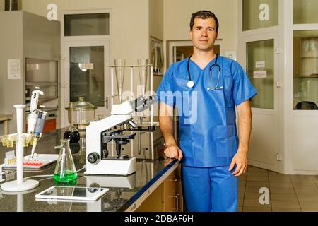 Medico di sesso maschile o tecnico di laboratorio che controlla o ricerca di campioni di virus covid 19 al microscopio per aiutare a scoprire la vaccinazione contro il coronavirus Foto Stock