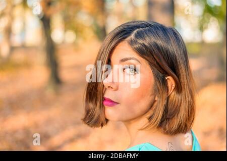 faccia di una bella giovane donna dai capelli neri semi-coperta dai capelli in una foresta gialla d'autunno Foto Stock