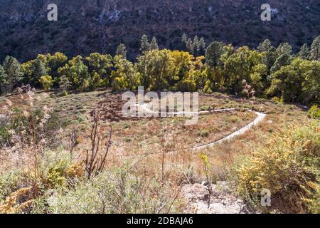 Persone irriconoscibili camminano su un sentiero che si snoda attraverso i resti di strutture murarie in Frijoles Canyon presso il Bandelier National Monument, New Mex Foto Stock