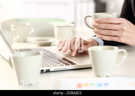 Primo piano di donne dirigenti che lavorano a mani in eccesso e che prendono la caffeina bere seduto su una scrivania in ufficio con il computer portatile Foto Stock