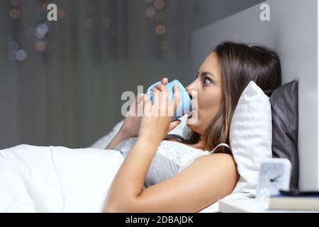 Insomniac donna bere caffè tazza con gli occhi spalancati sdraiati a letto di notte Foto Stock