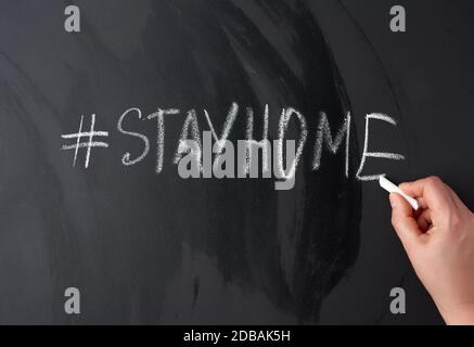 iscrizione rimanere a casa in gesso con un hashtag su una lavagna nera, concetto di auto-isolamento in un'epidemia e pandemica Foto Stock