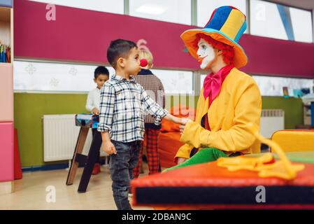 Clown divertente e bambino con naso rosso stanno giocando insieme. Festa di compleanno in sala giochi, baby Holiday nel parco giochi. Felicità infantile, l. Infantile Foto Stock