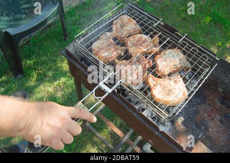 Primo piano di una mano dell'uomo che prepara carne fritta, all'aperto, in estate, sullo sfondo dell'erba Foto Stock