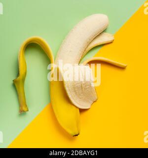 Banana pelata a metà su sfondo verde e giallo Foto Stock
