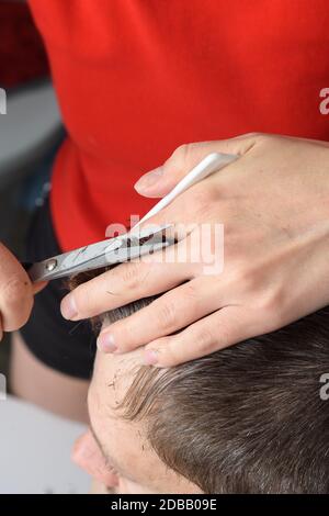 La moglie taglia i capelli sulla testa del marito a casa nel bagno Foto Stock