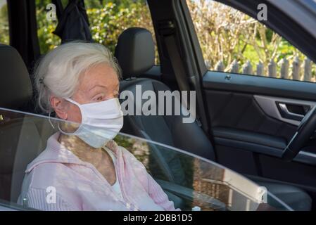 Donna anziana con maschera protettiva seduta in auto Foto Stock